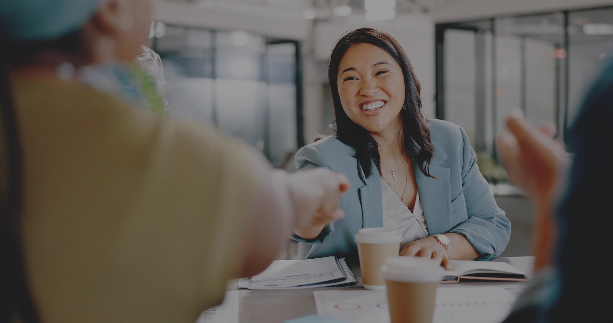 Two women sitting at a modern table talking with a city view behind them.